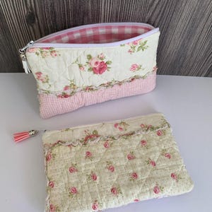 Peut inclure: Deux pochettes matelassées à fermeture éclair en tissu crème à motif floral de roses roses et en tissu à carreaux vichy rose clair et blanc. Chaque pochette comprend une fermeture éclair blanche et un pompon rose décoratif sur la tirette.
