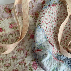 May include: Quilted tote bag with floral patterns in pink, white, and blue. The bag features a patchwork design with various floral prints and a light pink strap with a delicate floral pattern.