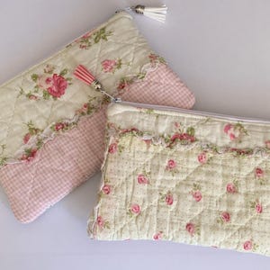 May include: Two quilted cosmetic bags with floral and gingham patterns. One bag features a cream background with pink roses, while the other has a cream background with pink roses and a pink gingham bottom. Both have a zipper closure and tassel.