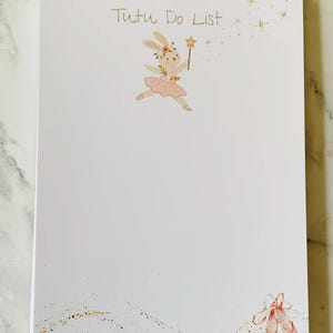 May include: A white notepad with the text Tutu Do List at the top. It features a cartoon rabbit wearing a pink tutu and floral crown, holding a gold star wand. The bottom right corner displays a pair of pink ballet slippers with gold glitter accents.