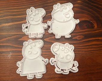 May include: Four white plastic cookie cutters shaped like cartoon pigs. The cutters are in the shape of a pig with a curly tail, a pig with a straight tail, a pig with a curly tail and a pig with a straight tail.