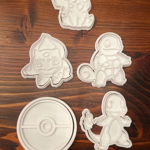 Peut inclure: Cinq emporte-pièces en plastique blanc en forme de personnages Pokémon : Pikachu, Carapuce, Bulbizarre, Salamèche et une Poké Ball.