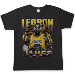 Könnte beinhalten: Schwarzes T-Shirt mit einem Aufdruck des Basketballspielers LeBron James, der ein lila-goldenes Lakers-Trikot trägt und einen Basketball hält. Der Text "LEBRON JAMES" ist in Gelb über und unter dem Bild gedruckt.