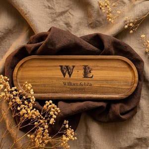 May include: A wooden serving tray with rounded edges. The tray is engraved with the initials "W & L", floral accents, the names "William & Léa", and the date "06.03.2025". The tray is a warm brown color.