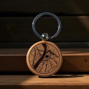 May include: A circular wooden keyring with a silver ring. The keyring displays a detailed map design with a heart symbol. The wood has a natural grain and a dark engraved map pattern.