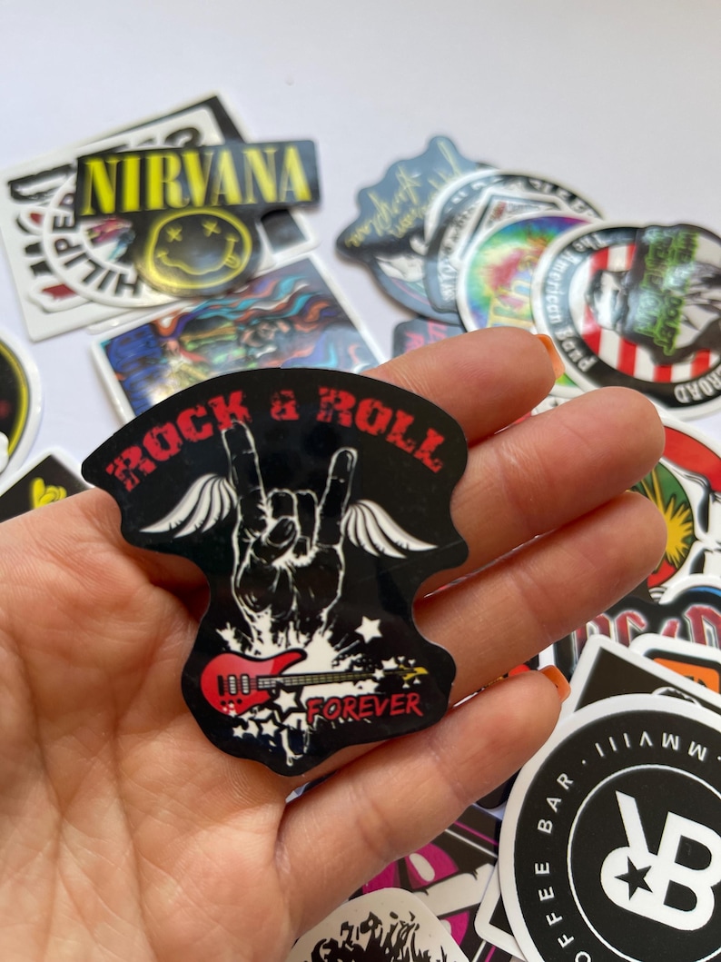 May include: A black and red sticker with the words "Rock & Roll" and "Forever" on it. The sticker features a hand with a guitar and wings.