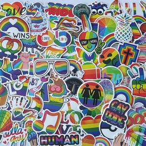 May include: A collection of colorful stickers with rainbow and LGBTQ+ pride themes. The stickers feature various designs, including rainbows, hearts, sunglasses, and text like "LOVE," "GAY," and "WINS."