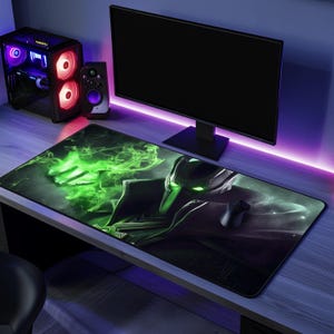 May include: A black and green gaming mouse mat with a green and black character design. The mouse mat is on a desk with a computer monitor, speakers, and a keyboard.