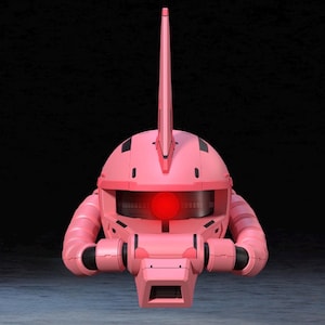 Op de afbeelding: Een roze robothoofd met een opvallende antenne en een gloeiend rood oog. De kop heeft een afgeronde vorm met zwarte accenten en buisvormige structuren aan de zijkanten. De achtergrond is donker en effen.