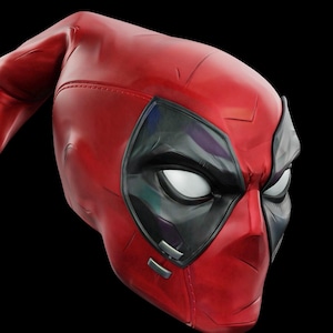 May include: A red and black Deadpool mask. The mask is primarily red with black accents around the eyes. The eyes are white. The mask is made of a smooth material and has a detailed design.