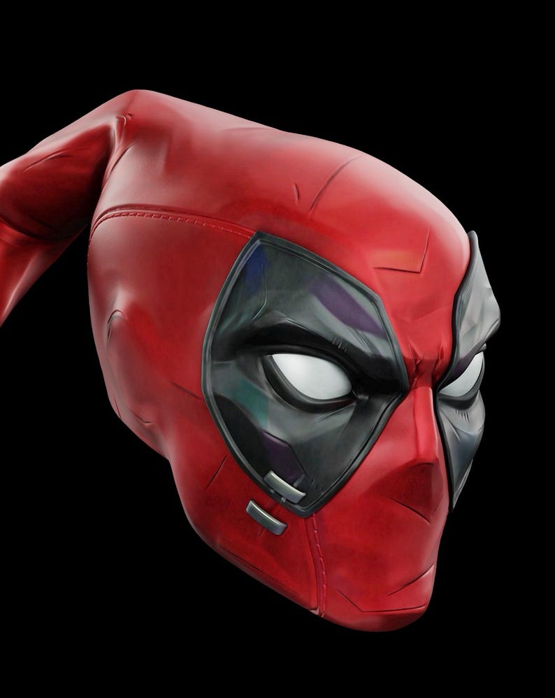 May include: A red and black Deadpool mask. The mask is primarily red with black accents around the eyes. The eyes are white. The mask is made of a smooth material and has a detailed design.