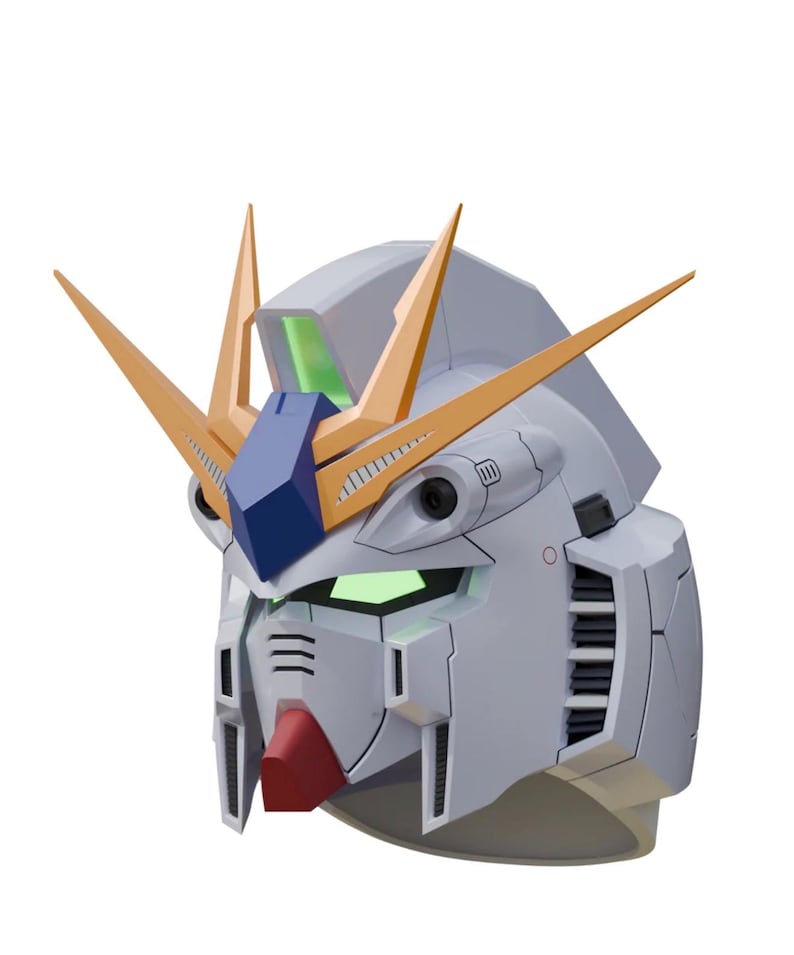 May include: A detailed, light gray Gundam head model with gold and blue accents. The model features a red chin, green glowing eyes, and multiple vents and panels. The head has two prominent gold V-fins.