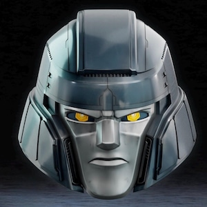May include: A metallic gray robot head with yellow eyes. The head has a detailed design with angular features and a stern expression. The robot head is a collectible item, possibly a toy or a decorative piece.