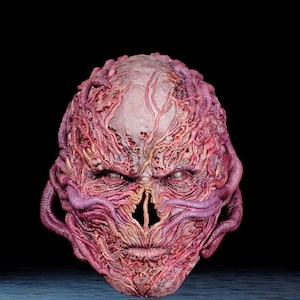 May include: A grotesque mask with a pale, textured surface, detailed with red and purple veins and tendrils. The mask has a menacing expression with hollow eye sockets and a slit for a mouth, creating a disturbing and unsettling appearance.
