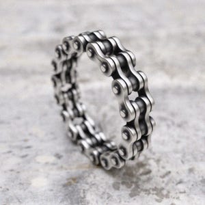 Puede incluir: Un anillo de plata hecho de una doble fila de cadena de bicicleta enlazada.