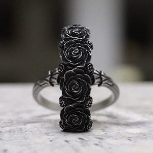 May include: A silver ring with a design of five black roses. The roses are arranged vertically and are detailed with intricate carvings.