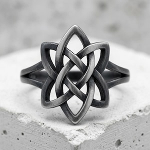 Op de afbeelding: Een donker zilverkleurige ring met een centraal zespuntig stermotief, gevormd door een ingewikkeld, doorlopend vlechtpatroon. Het metalen oppervlak heeft een geborstelde, matte afwerking met donkere verdiepte delen in het ontwerp.