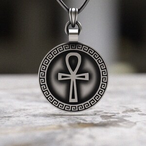 May include: Silver pendant necklace featuring an Ankh symbol with a Greek key border. The pendant is round and has a black and white design.
