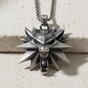 May include: A silver-toned metal pendant shaped like a stylised wolf head with an open mouth, featuring sharp geometric angles and a dark oxidised finish. The pendant hangs from a matching silver-toned metal ball chain necklace.