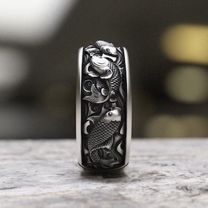 May include: A silver ring featuring a detailed design of three koi fish swimming in a swirling pattern.