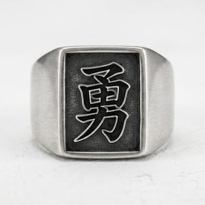 Könnte beinhalten: Ein silberfarbener Siegelring mit rechteckiger Front und gebürsteter Metalloberfläche. In der Mitte des Rings befindet sich eine vertiefte, dunkel getönte rechteckige Einlage, die mit dem japanischen Kanji für Mut, 勇, in einem kräftigen Stil graviert ist.