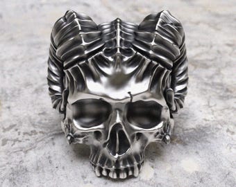 May include: A silver skull ring with horns. The skull is detailed with a textured surface and the horns are curved and pointed.