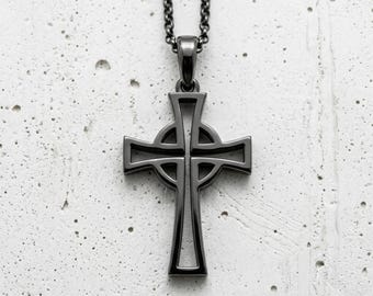 Pode incluir: Colar com pingente de cruz celta cinza escuro. O pingente apresenta um design de cruz detalhado com um centro circular e é suspenso por uma corrente correspondente. O colar é exibido em um fundo texturizado cinza claro.