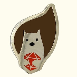 May include: A silver pin with a white cartoon animal holding a red gemstone. The animal has a brown background.