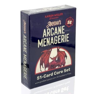 May include: A blue box with a red and white illustration of a creature with wings. The box says "Akasha's Arcane Menagerie 51-Card Core Set" and includes the website address www.goodberrypress.com.