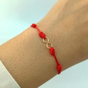 Könnte beinhalten: Rotes Armband mit einem goldenen Unendlichkeits-Anhänger.