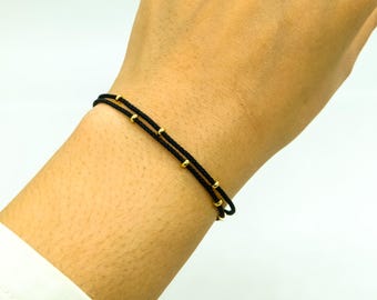 May include: A black cord bracelet with gold beads. The bracelet is double-layered and has a simple design.