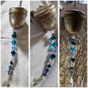 Puede incluir: Un colador de té de plata con una cadena y una guirnalda de cuentas de cristal azul colgando de él.