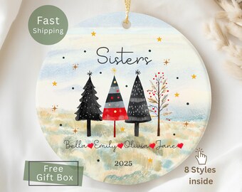 May include: A round Christmas ornament with a watercolor design featuring four stylized trees. The word "Sisters" is above the trees, with names and the year 2025 below. The ornament has a gold string for hanging.