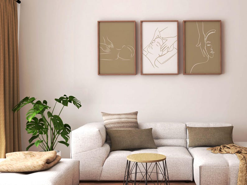 May include: Three framed line art prints depicting a person receiving a massage. The prints are in brown frames and have a beige background. The prints are hung on a white wall above a white couch with brown throw pillows.