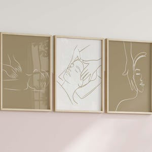 May include: Three framed illustrations of line drawings of people receiving a facial massage. The illustrations are in a minimalist style and are printed on a beige background.