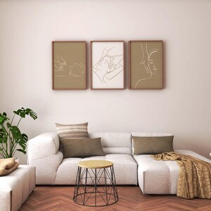 May include: A white sectional sofa with three pillows and a throw blanket. The sofa is in front of a white wall with three framed line drawings of people. A small black wire table sits in front of the sofa.