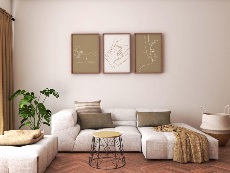 May include: A white sectional sofa with three pillows and a throw blanket. The sofa is in front of a white wall with three framed line drawings of people. A small black wire table sits in front of the sofa.