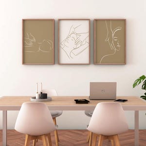 May include: Three minimalist line art prints depicting a person receiving a massage. The prints are framed in light brown wood and hung on a white wall above a wooden table with a laptop and two chairs.