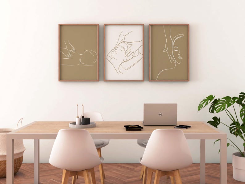 May include: Three minimalist line art prints depicting a person receiving a massage. The prints are framed in light brown wood and hung on a white wall above a wooden table with a laptop and two chairs.
