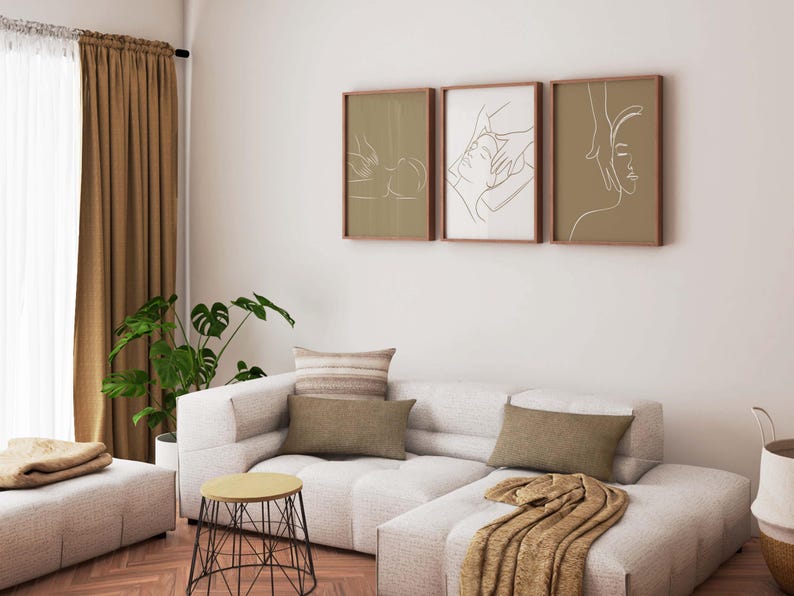 May include: A white sectional sofa with brown throw pillows and a brown blanket. Three framed line drawings of people receiving a massage hang on the wall above the sofa.