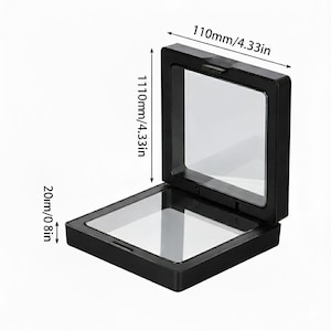 May include: A black display case, open to reveal a clear interior. The case measures 4.33 inches wide, 4.33 inches tall, and 0.8 inches deep. The case has a hinged lid and is designed to showcase small items.