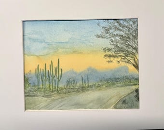 May include: Watercolor painting of a desert landscape with a road leading into the distance. The sky is a pale blue with a yellow sunset in the background. There are several tall cacti in the foreground.