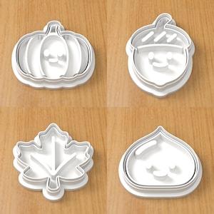 Op de afbeelding: Een set van vier witte plastic koekjesvormen met herfstthema, waaronder een pompoen, een eikel, een esdoornblad en een kastanje, elk voorzien van interne details om gezichtjes of bladnerven in het deeg aan te brengen.