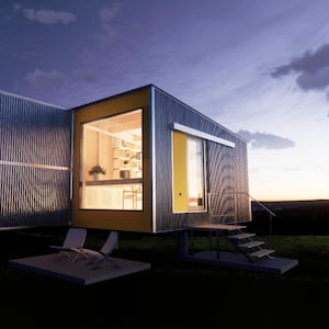 May include: A small, modern, yellow and gray house with a large window and a deck with two chairs. The house is lit up at night and the sky is dark.