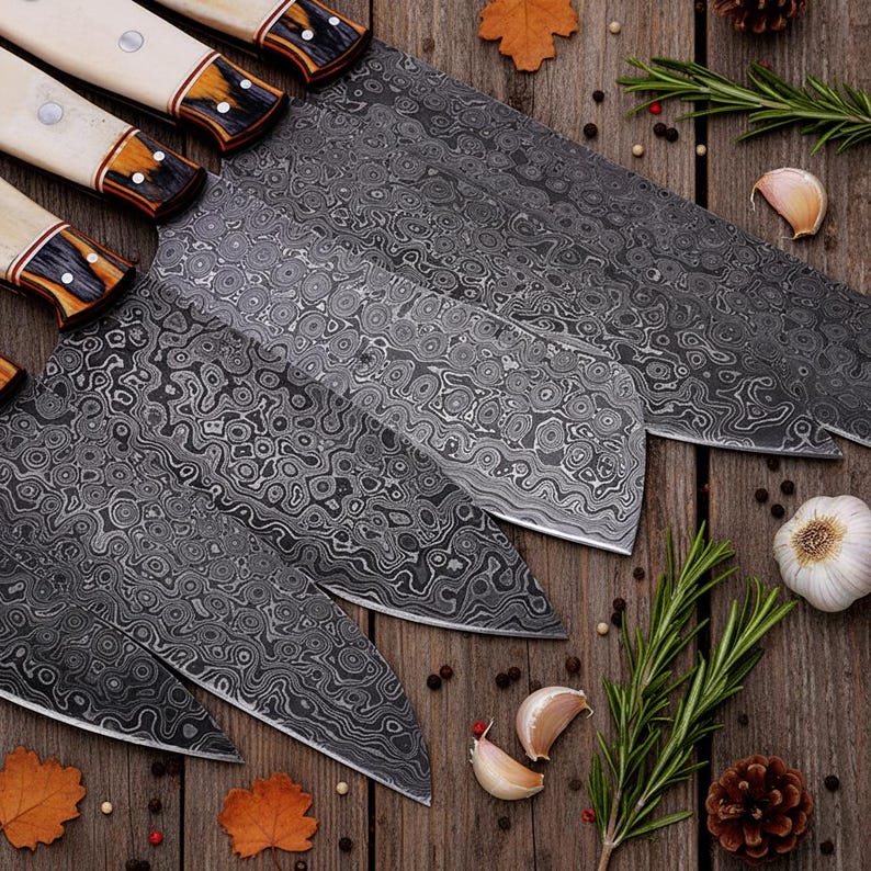 May include: A set of five Damascus steel kitchen knives with patterned blades and cream-colored handles. The blades have a unique, swirling design. The handles are accented with dark brown and gold details. The knives are arranged on a wooden surface.