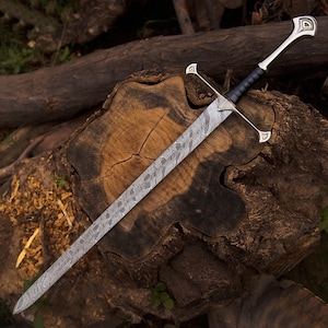 May include: A long sword featuring a double-edged blade with a distinct wavy Damascus steel pattern. The hilt includes a metallic crossguard with triangular accents, a black leather-wrapped grip, and a matching metallic pommel with a triangular design.