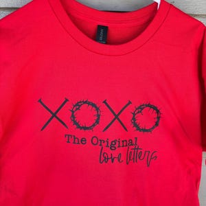 Espalhe amor e positividade com nossa camiseta XOXO. Esta camiseta vermelha vibrante exibe um design charmoso 'XOXO The Original Love Letters'.