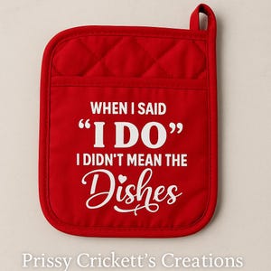 May include: Red quilted oven mitt with the text "WHEN I SAID 'I DO' I DIDN'T MEAN THE Dishes" in white. The mitt has a pocket and a loop for hanging. The text is in a playful font.