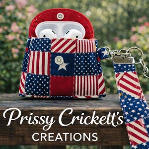 May include: A patriotic AirPod case with a matching wrist strap. The case is made of red, white, and blue fabric, featuring stars and stripes. The case is open, revealing white earbuds. The text "Prissy Crickett's CREATIONS" is at the bottom.