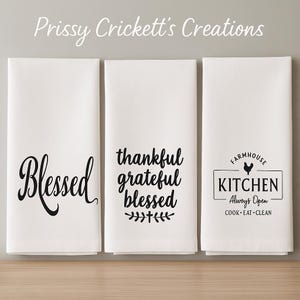 May include: Three white kitchen towels with black text. One towel says "Blessed", another says "thankful grateful blessed", and the third says "Farmhouse Kitchen Always Open Cook Eat Clean" with a rooster graphic. The brand name "Prissy Crickett's Creations" is at the top.